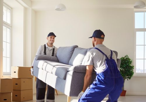 Cheerful,Man,Movers,Carrying,A,Sofa,During,A,Relocation,To